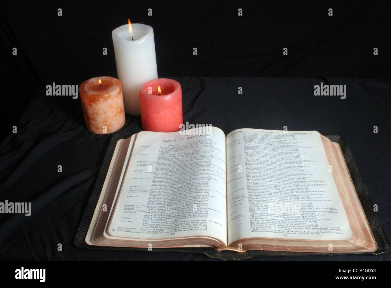 A Bible is open with three candles burning at the top left corner Stock