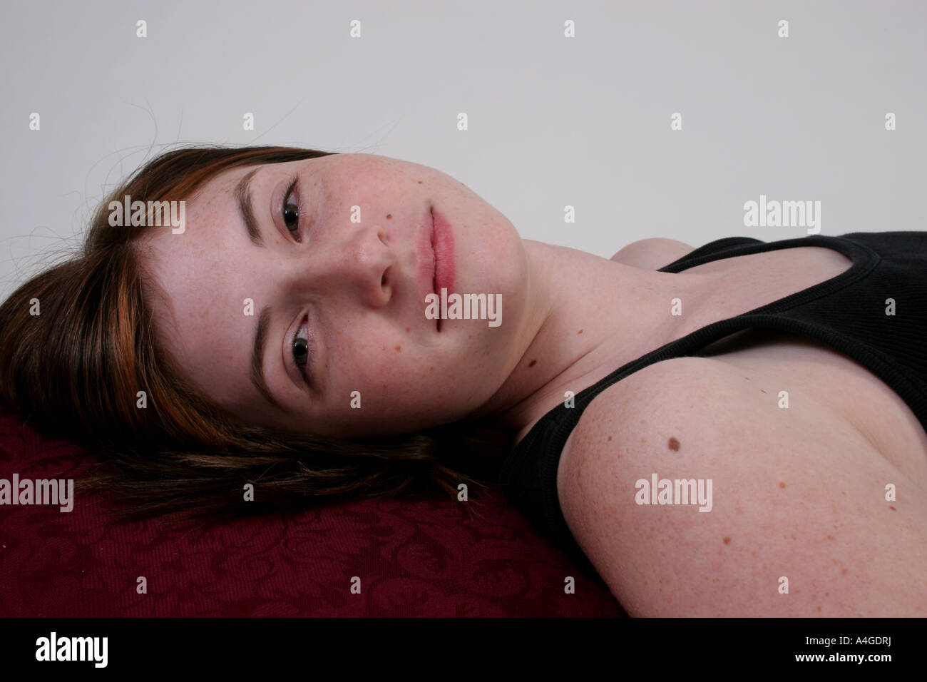 A woman in a black top is laying down and looking at the camera with a whimiscal smile. Stock Photo