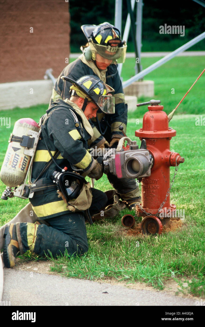 Two fire fighters putting a hose connection on a hydrant to deliver water to the pumper engine for a fire Stock Photo