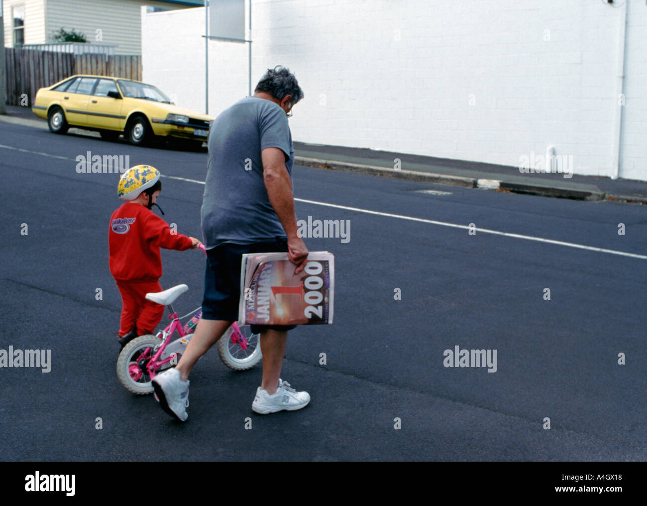 A man and child crossing the street with the newspaper showing the headlines for New Years day January first 2000 1 1 2000 Stock Photo