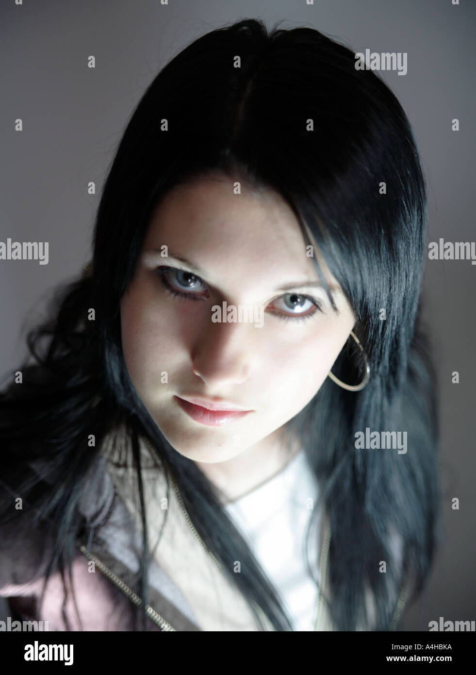 Young girl aged 16 with black hair upwards confident look with harsh blue light somewhat mystical Stock Photo