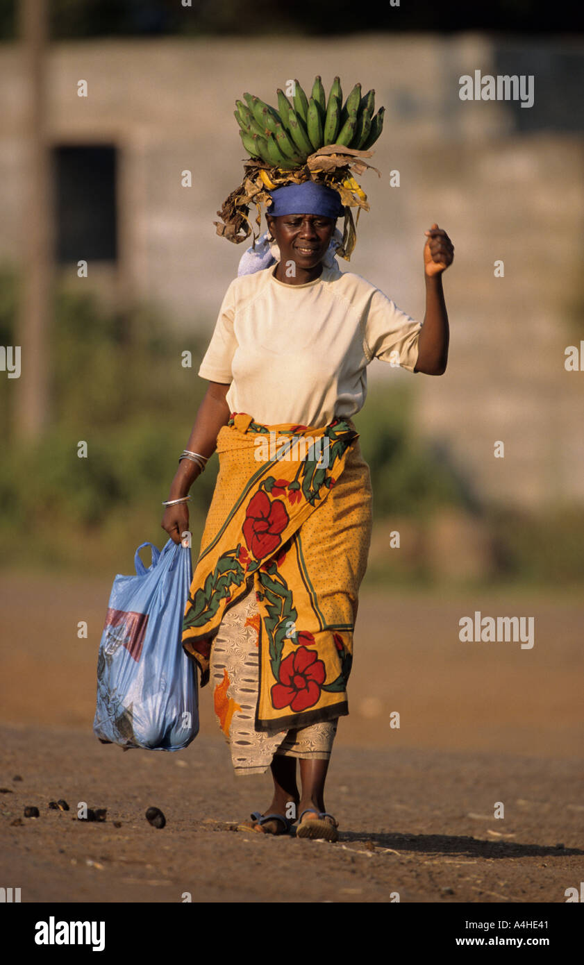 Woman returning form the market carrying a plastic bag and a bunch of cooking bananas on her head, Moshi, Tanzania Stock Photo