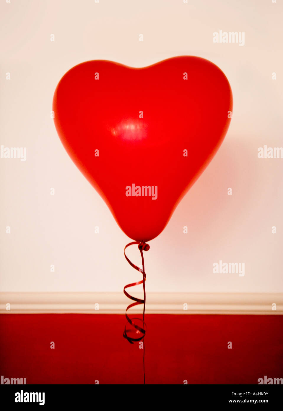 Red heart shaped balloon against a red and white wall Stock Photo - Alamy