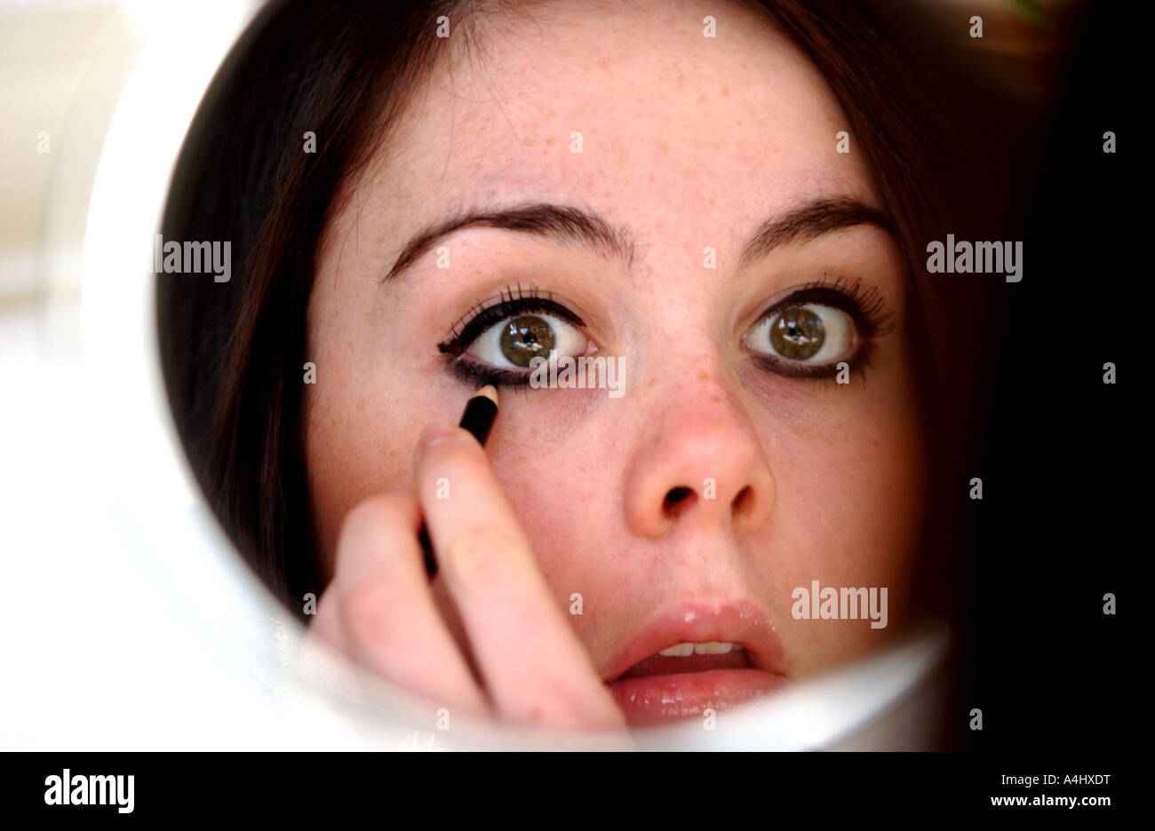 Brunette model young girl teenage applying eye makeup in mirror Stock Photo
