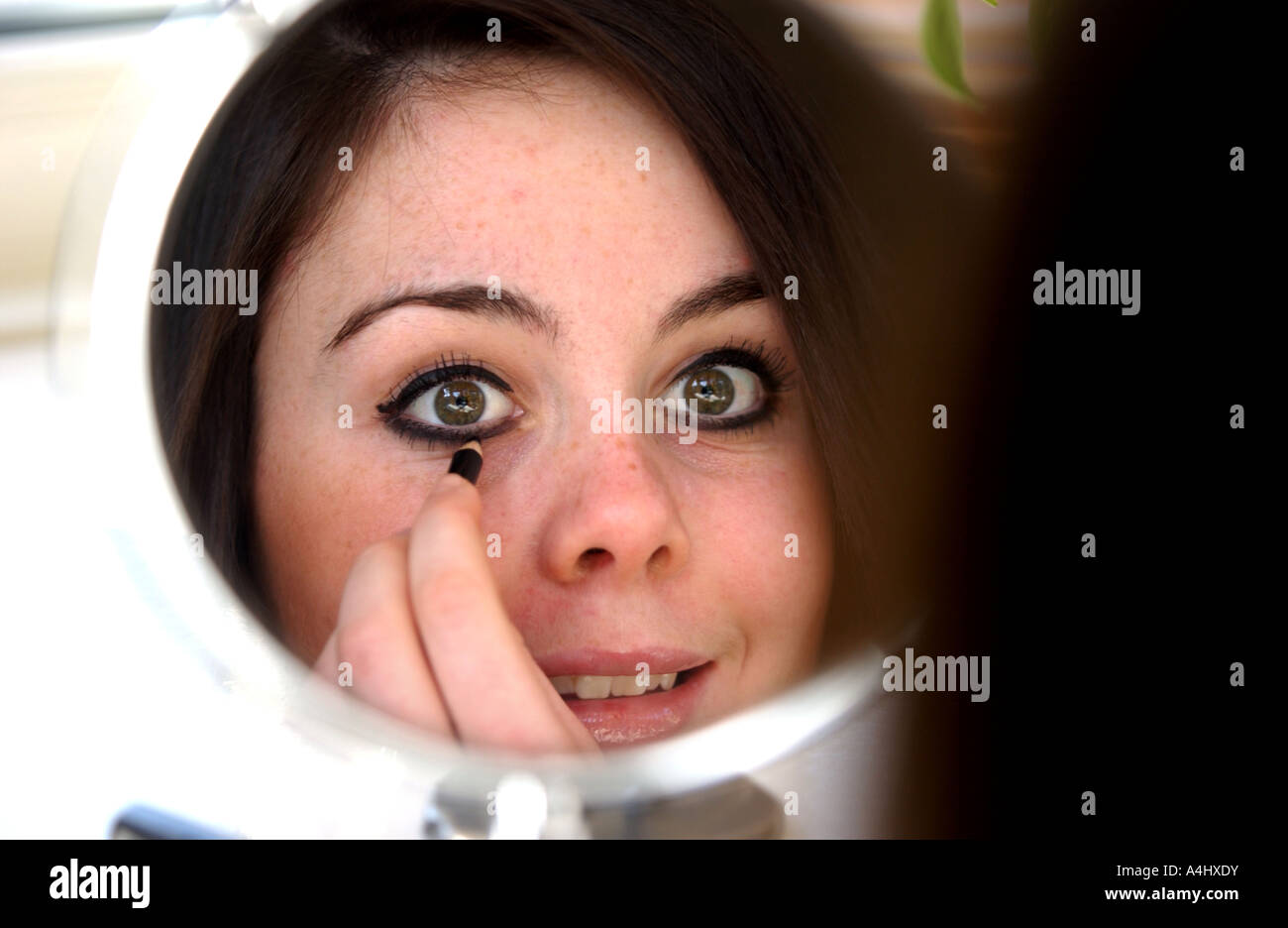 Brunette young girl teenage applying eye makeup in mirror Stock Photo