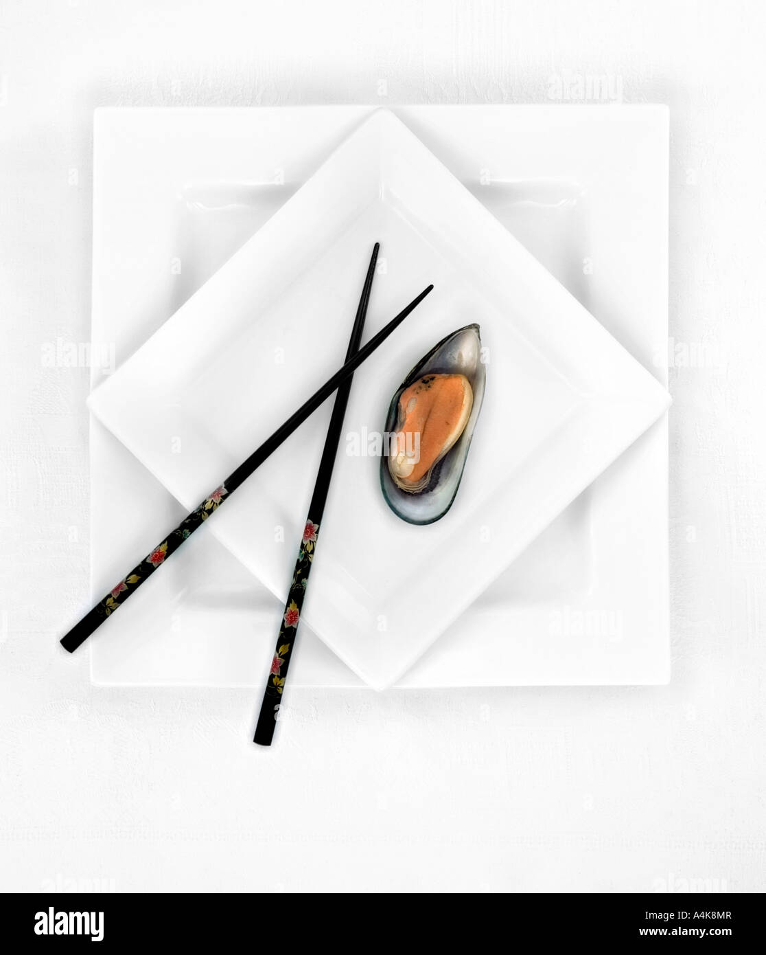 Pair of black chopsticks and one green shell mussel on a white plate Stock Photo