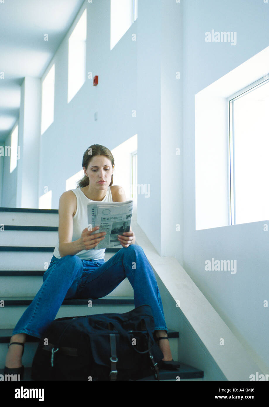 Woman sitting on stairs, reading newspaper, full length Stock Photo