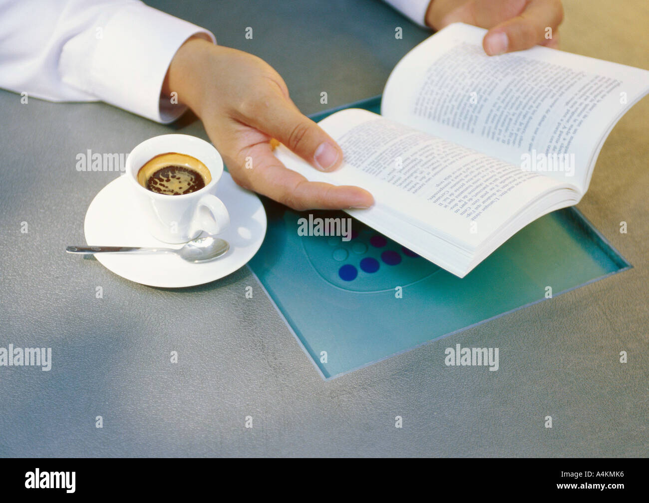 Man's hands holding book next to cup of espresso Stock Photo