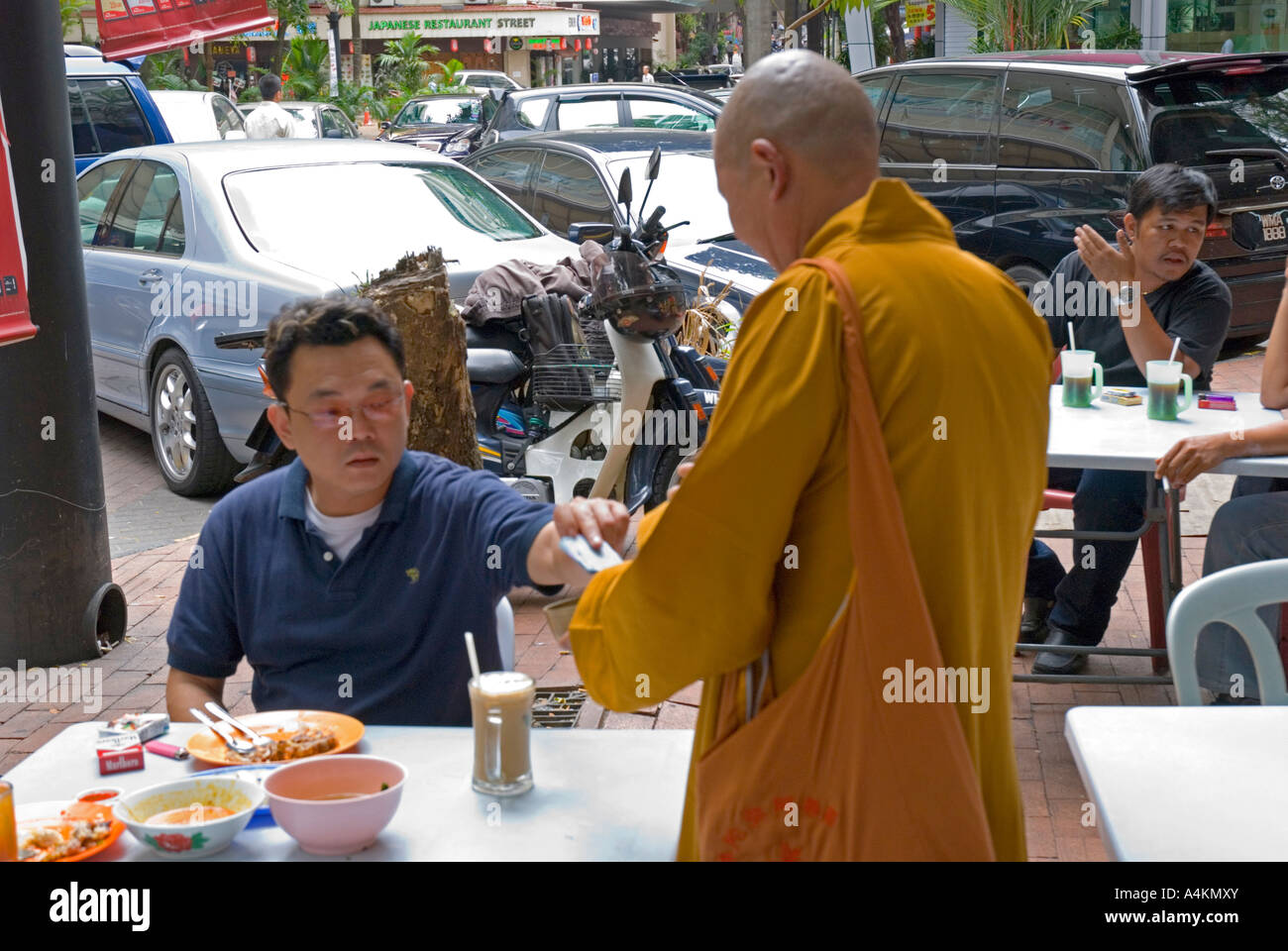 A diner at an outside restaurant in Kuala Lumpur makes a donation to a Buddhist monk Stock Photo