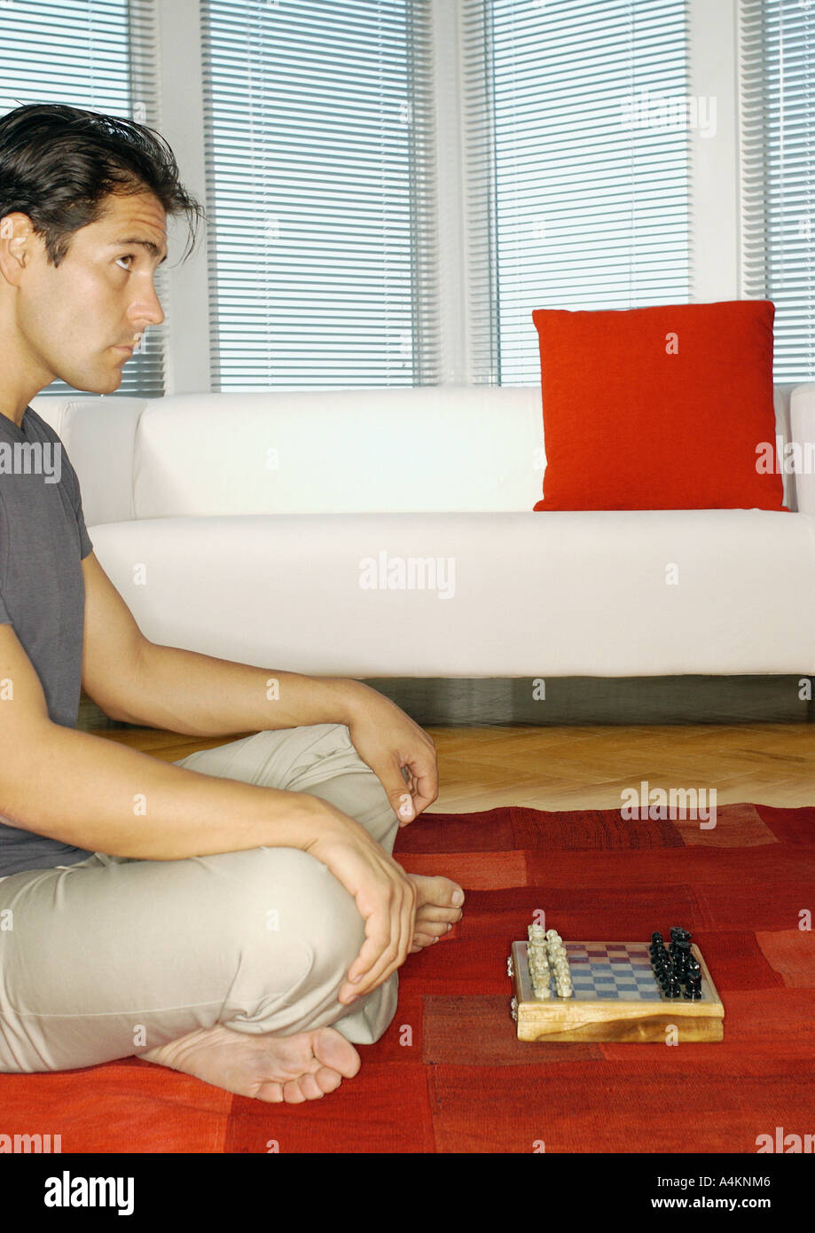 Man sitting on floor playing chess, side view Stock Photo