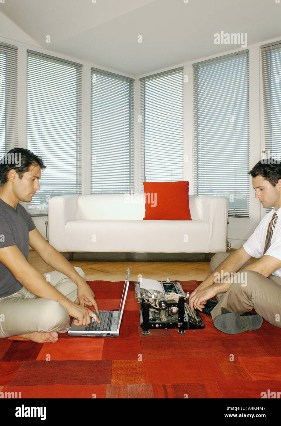 Man using laptop computer and second man using typewriter, side view Stock Photo
