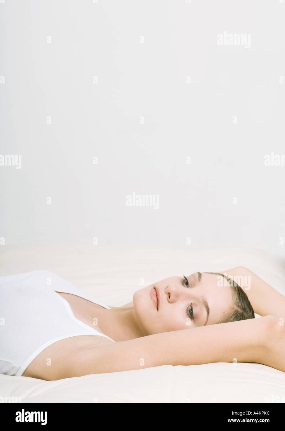 Woman lying back on bed with arms over head Stock Photo