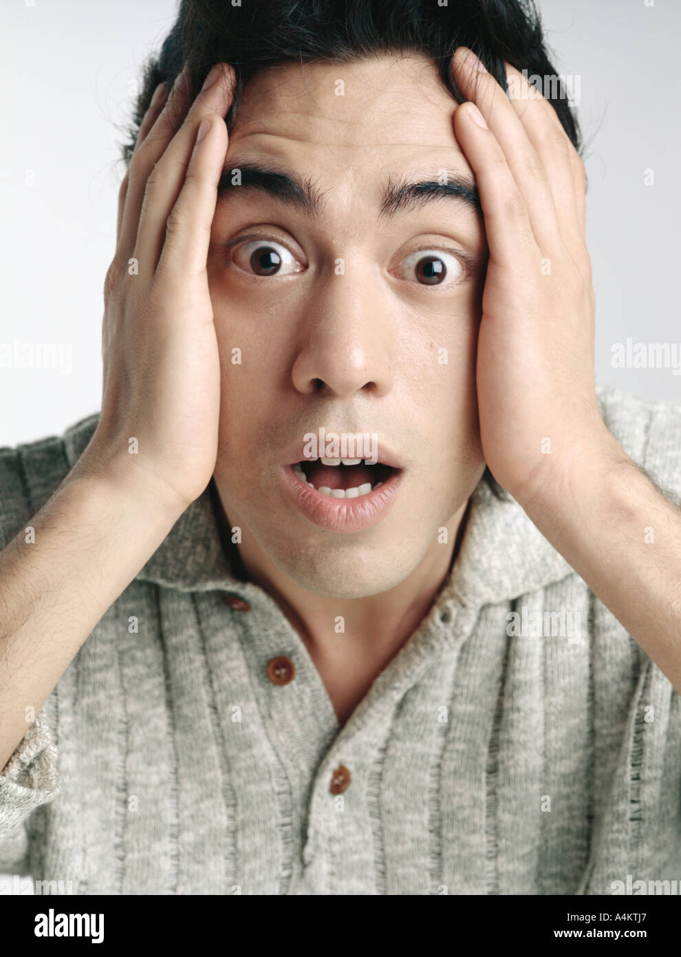 Man looking at camera with eyes wide open and eyebrows raised, holding face with hands Stock Photo