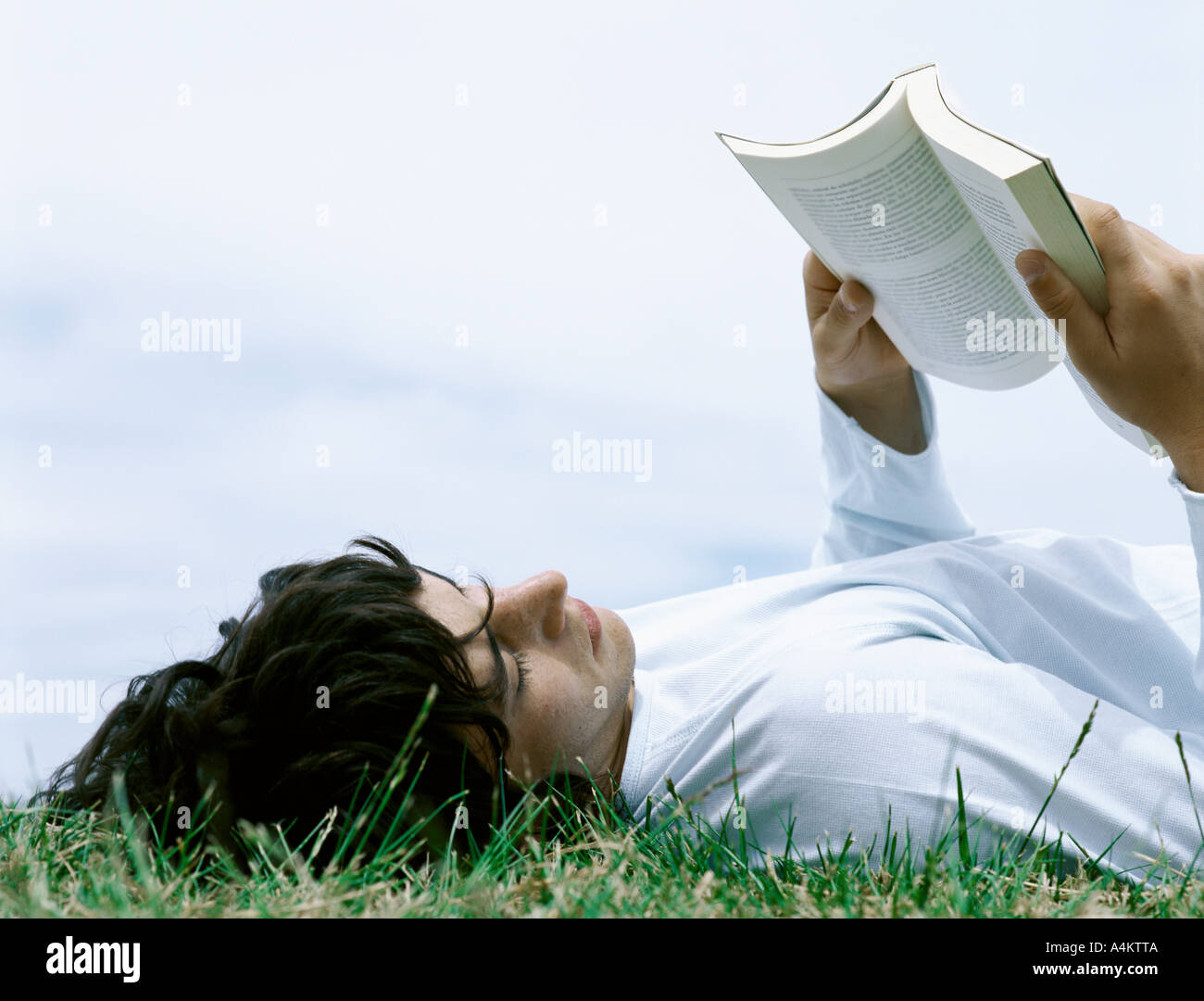 Young man lying on back in grass reading book, head and shoulders Stock Photo