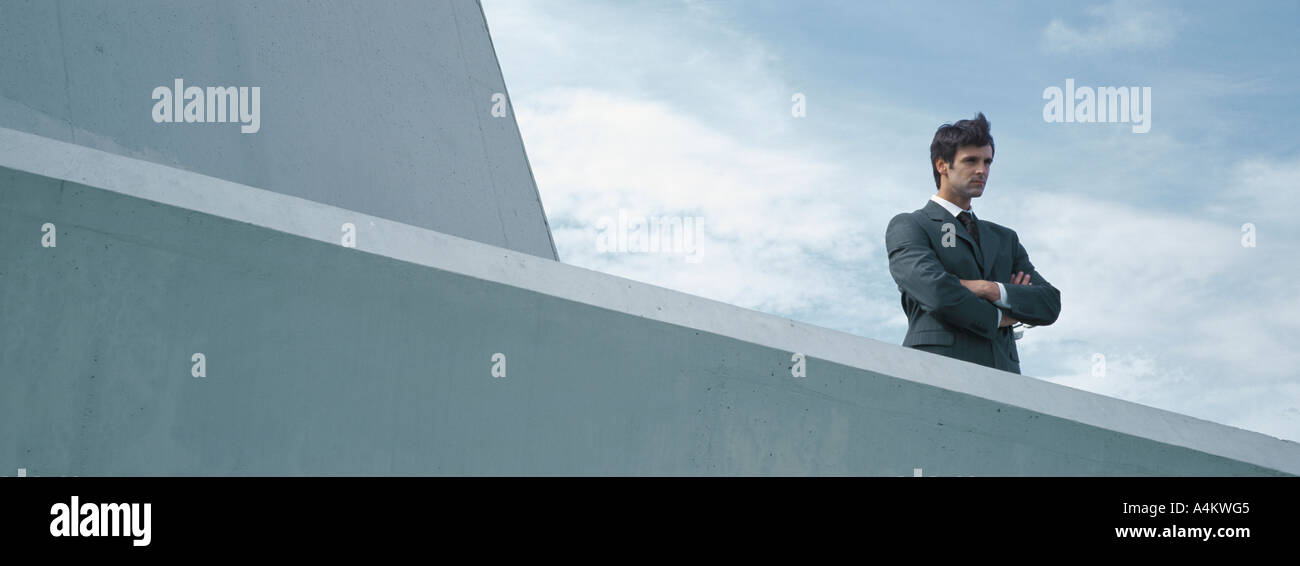 Man standing behind concrete wall with arms folded, low angle view Stock Photo