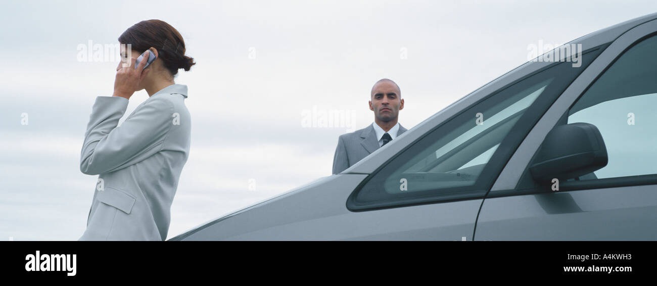 Woman and man in suits standing near car, man looking at camera, woman talking on cell phone Stock Photo