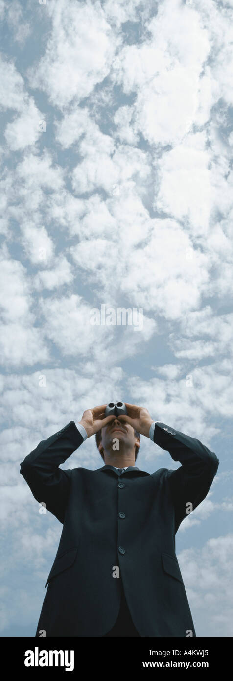 Man looking through binoculars, sky in background, low angle view Stock Photo