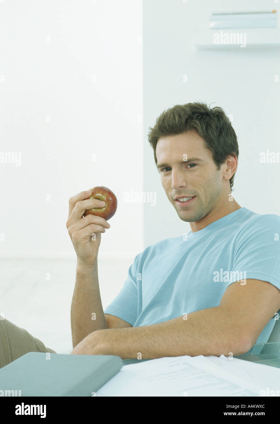 Young man sitting at table holding up apple in hand Stock Photo