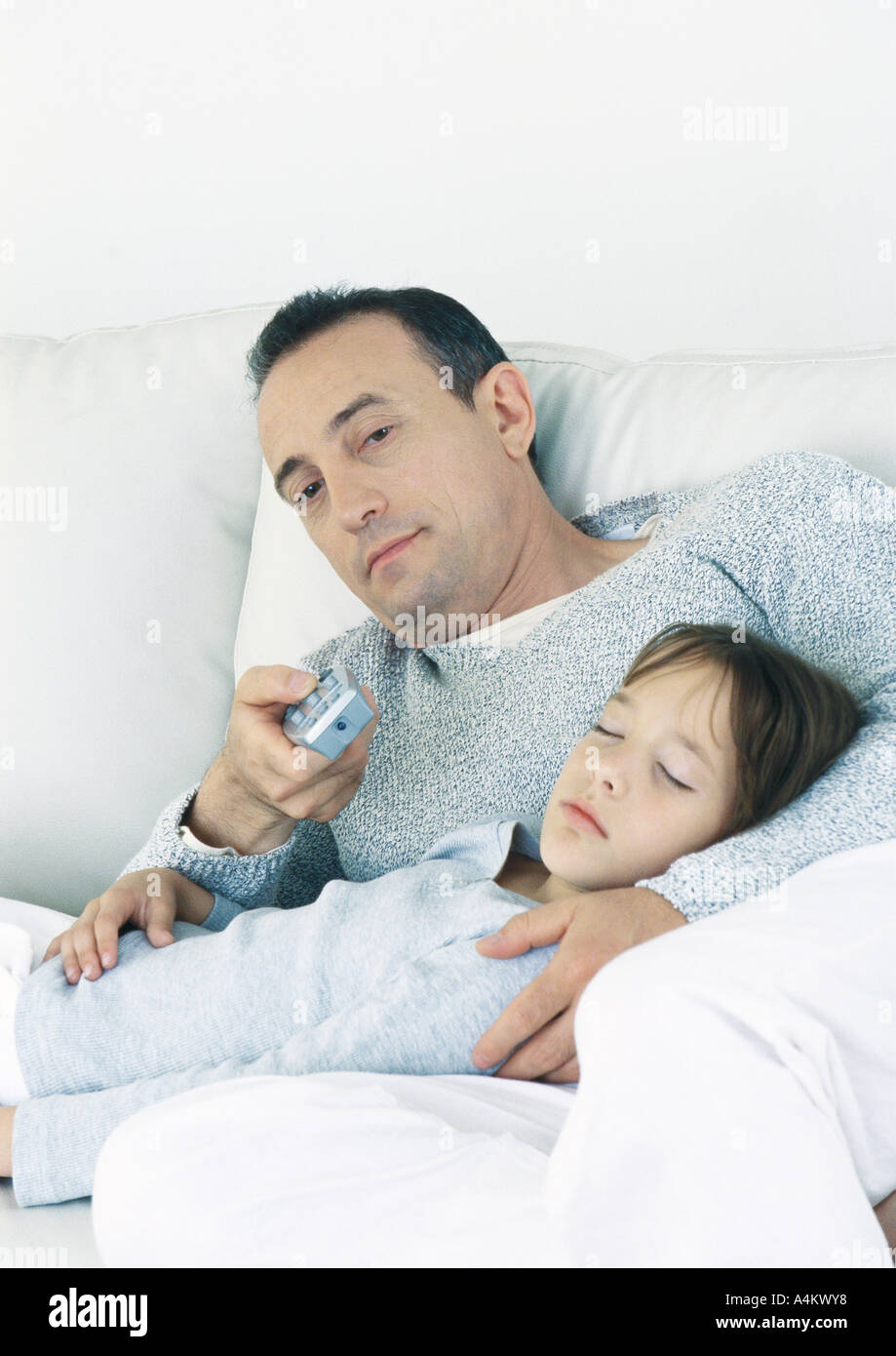 Man sitting on couch pointing remote control, holding sleeping daughter on lap Stock Photo