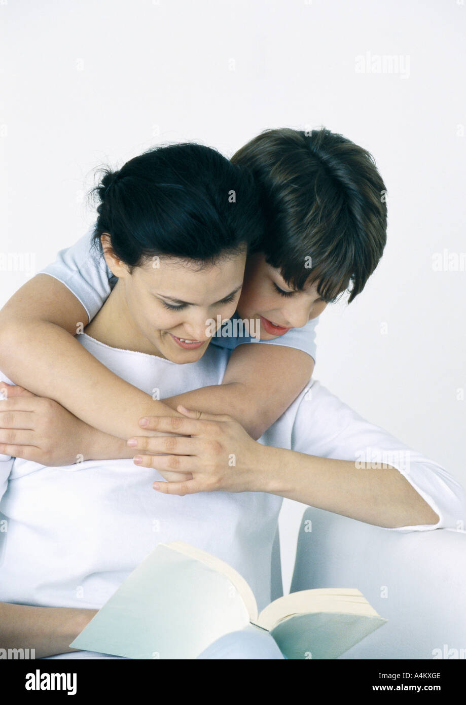 Woman and son reading book, boy with arms around woman, looking over her shoulder Stock Photo