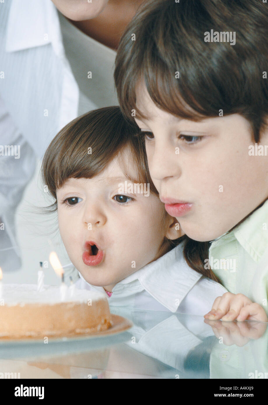 Boy and little girl blowing out candles on cake, mother in background Stock Photo