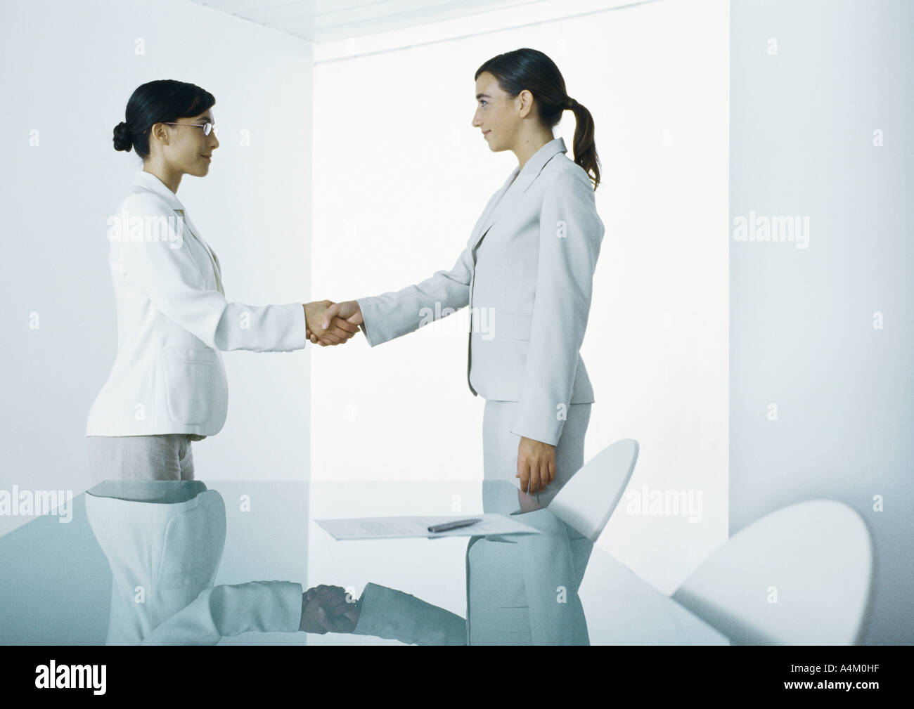 Two young women in suits shaking hands Stock Photo