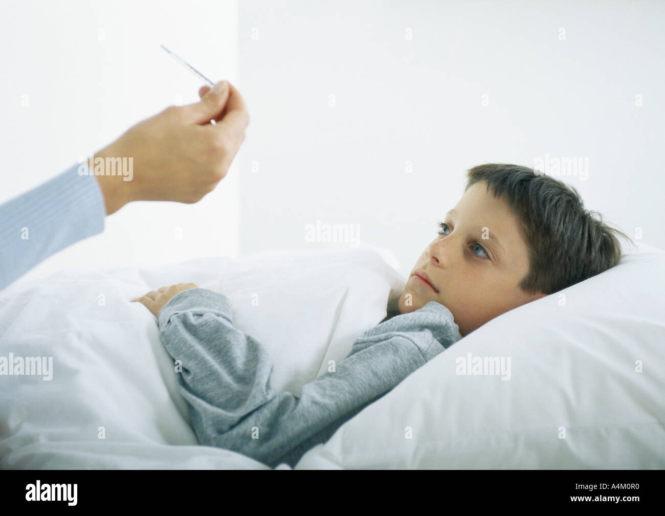 Boy in bed, woman's hand holding thermometer Stock Photo