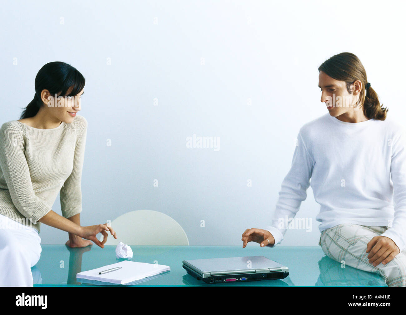 Man and woman sitting on table, woman flicking paper ball to man Stock Photo