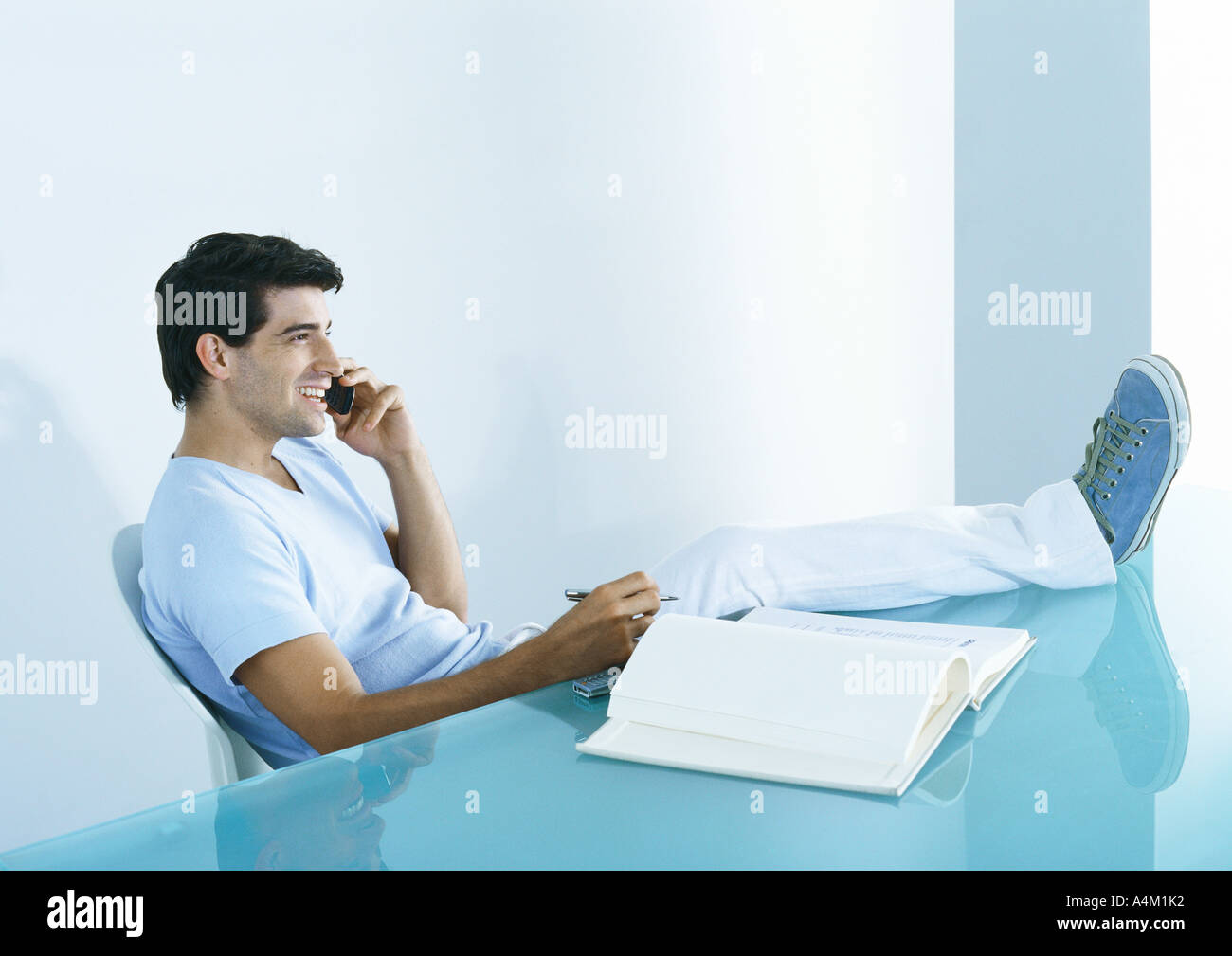 Man sitting at table with feet up, talking on phone Stock Photo