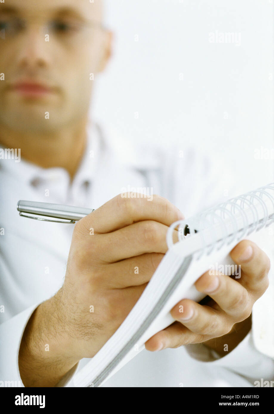 Man in white jacket taking notes, focus on hands in foreground Stock Photo