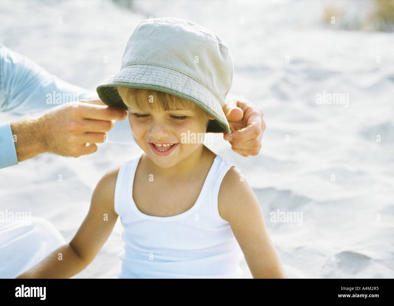 Father's hands putting hat on little boy, on beach Stock Photo