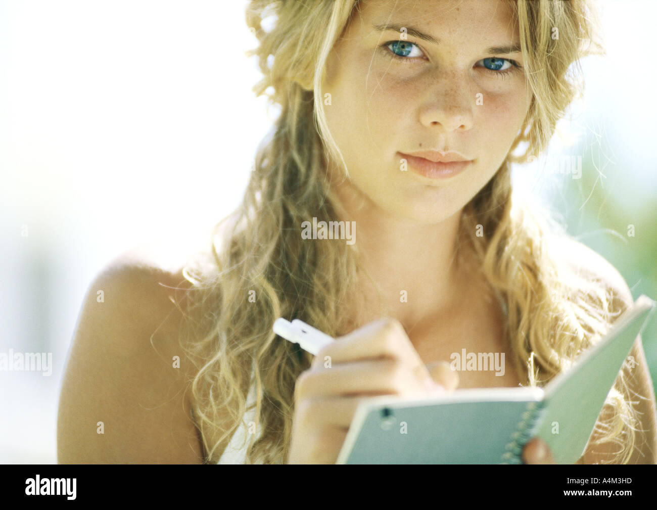Female student writing in notebook, looking at camera, close-up Stock Photo