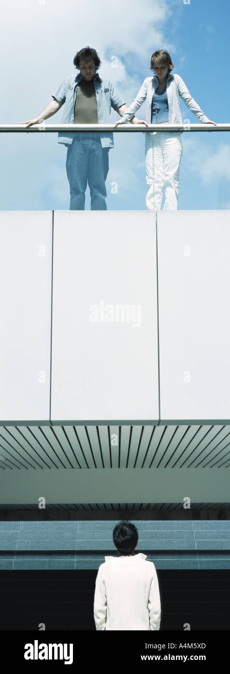 Young people standing on balcony looking down at young man Stock Photo