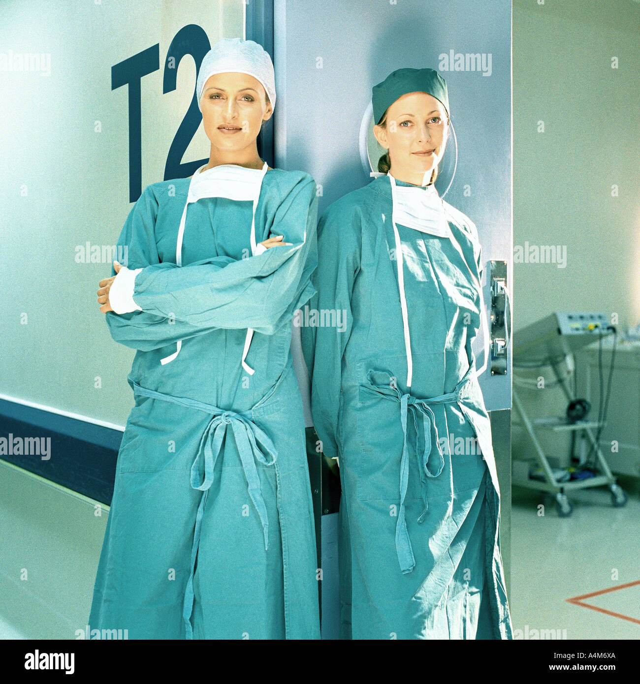 Two female doctors in operating gowns, leaning against doorframe Stock