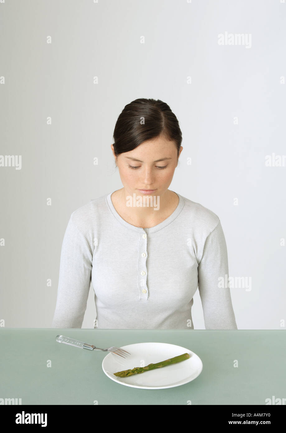 Young woman looking down at plate with single asparagus Stock Photo