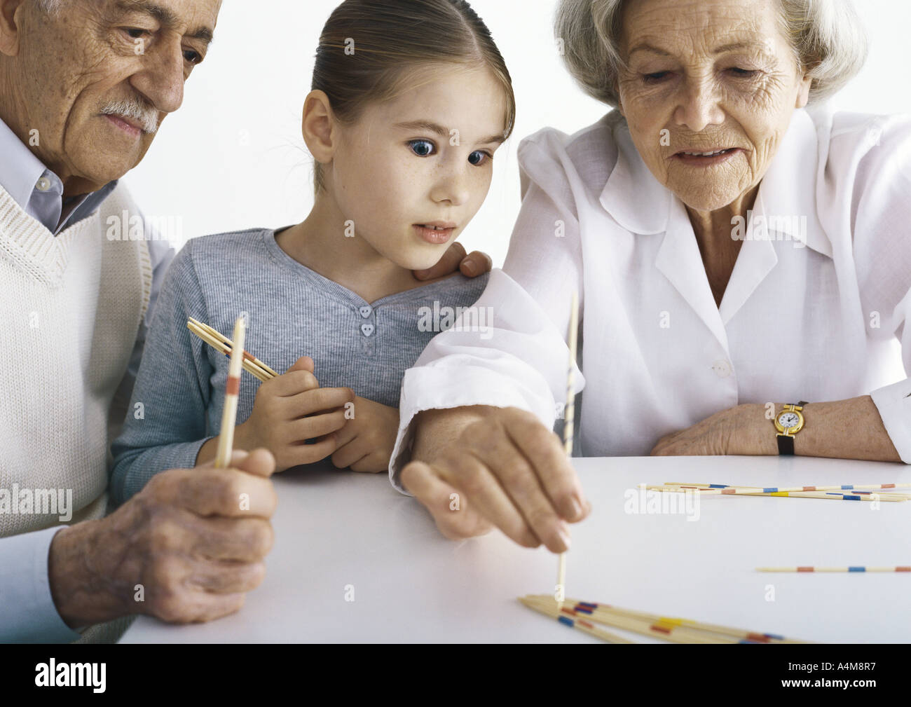 Grandparents and girl sitting at table playing pick up sticks Stock Photo