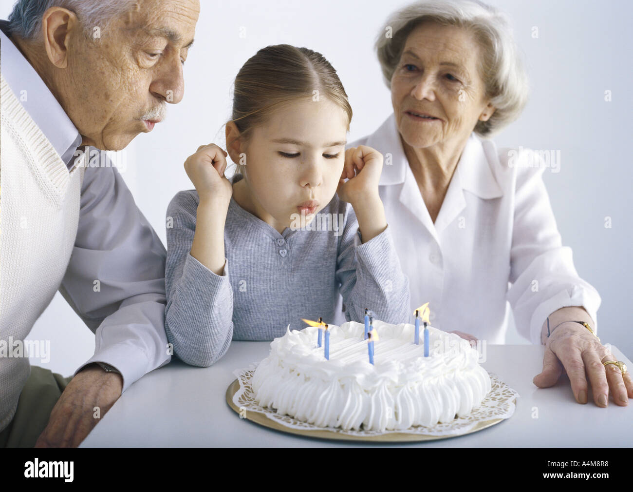 Girl sitting with grandparents, blowing out candles on cake Stock Photo