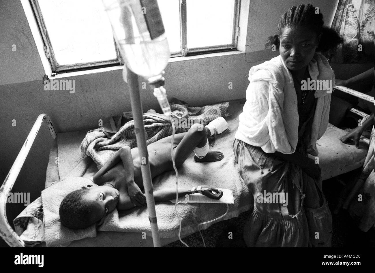 B/W of a young boy lying on a hospital bed with an amputated foot, having stepped on a landmine, with his mother. Adua, Ethiopia, Africa Stock Photo