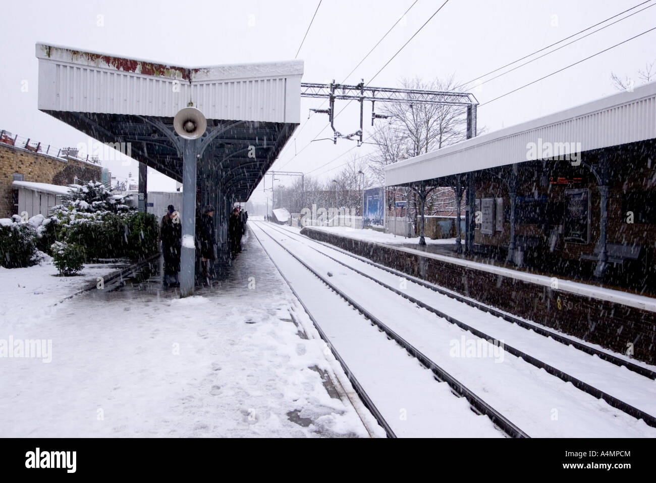 commuters wait on Train station platform in North East London with snow storm Stock Photo