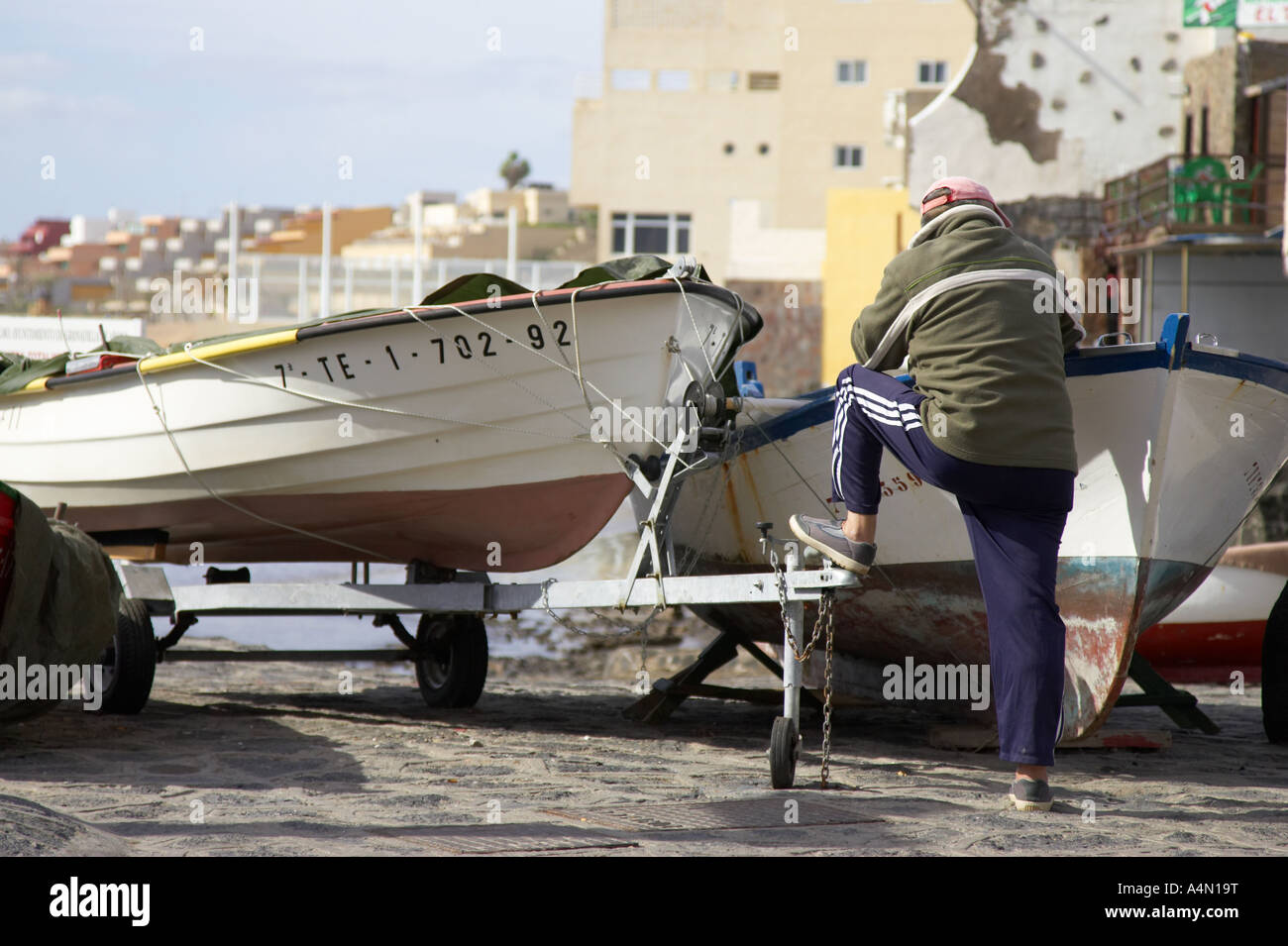 fisherman wearing fleece and cap stands beside old style fishing boats