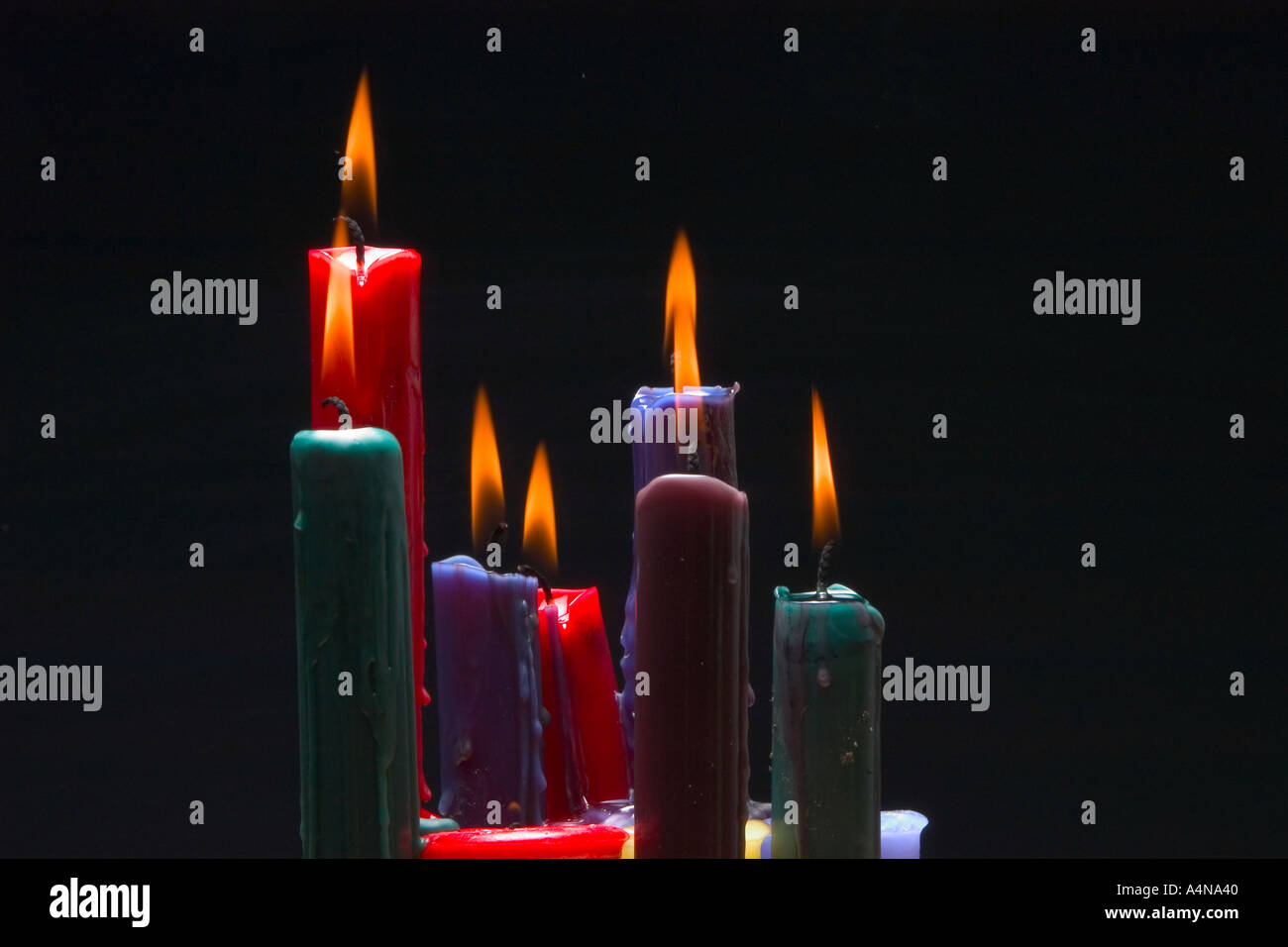 Multi colored candles burning against reflective black background Stock