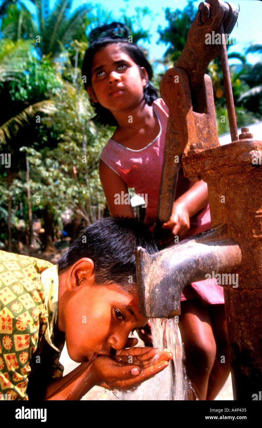 Young girl pumps well water for brother rural Bangladesh Stock Photo