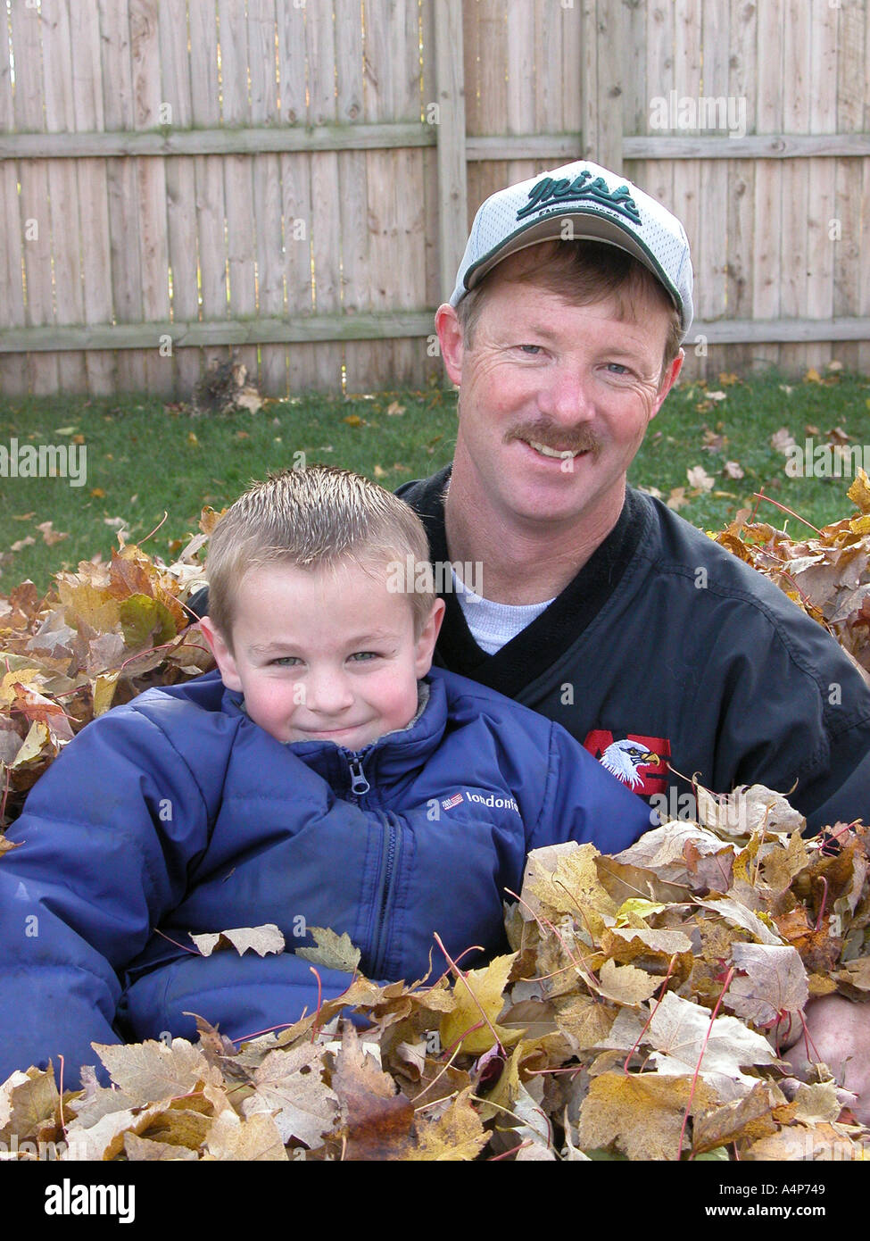 father and son pose for portrait in a pile of autumn leaves Stock Photo ...