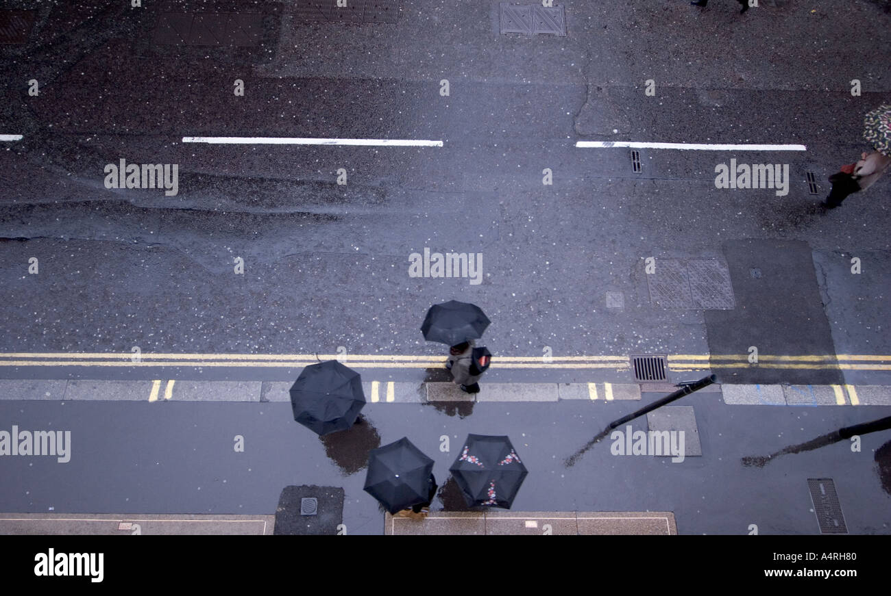 Shelter pedestrians walking in rain with umbrellas on pavement in London Street Stock Photo