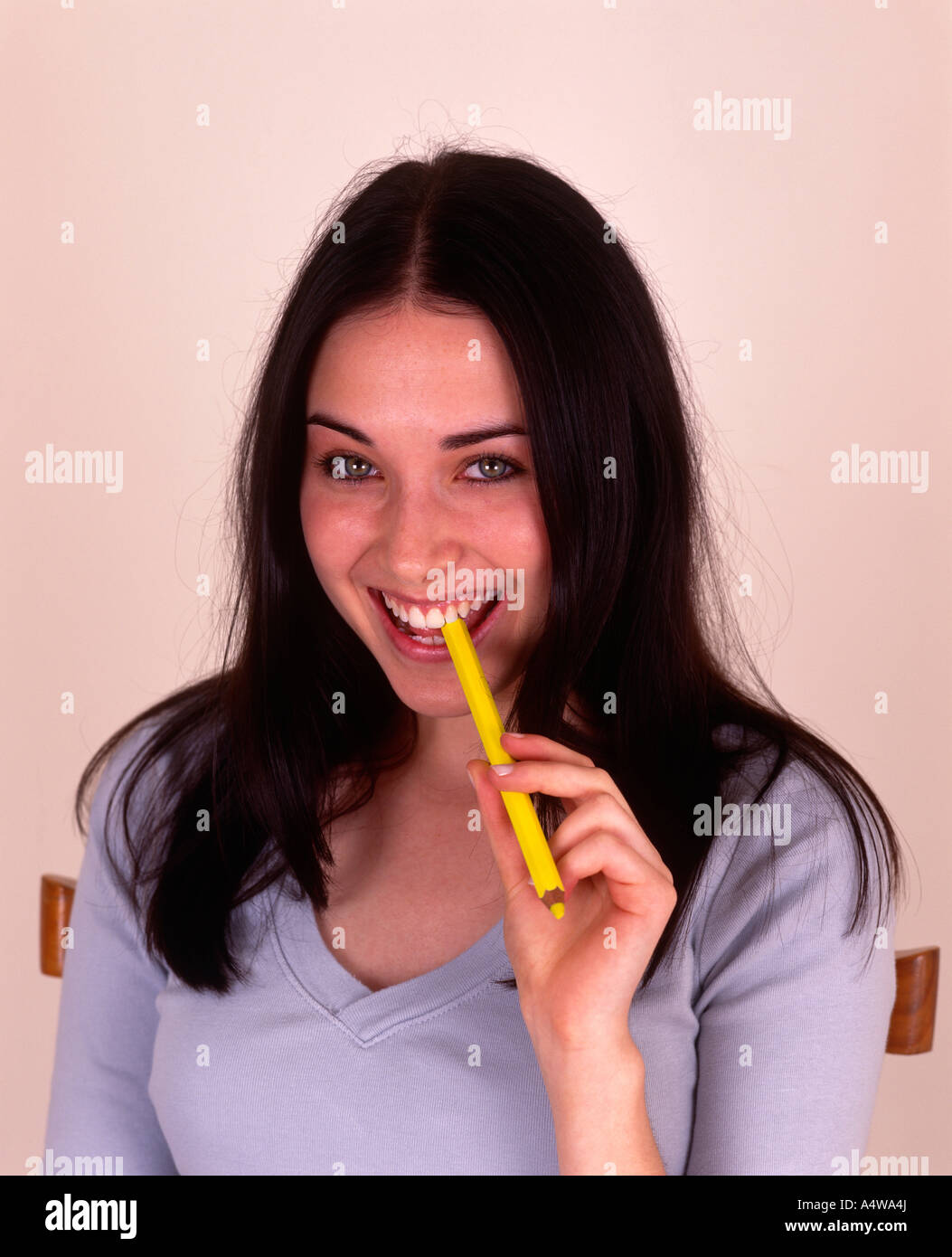 DARK HAIRED GIRL IN BLUE TOP YELLOW PENCIL TO MOUTH Stock Photo