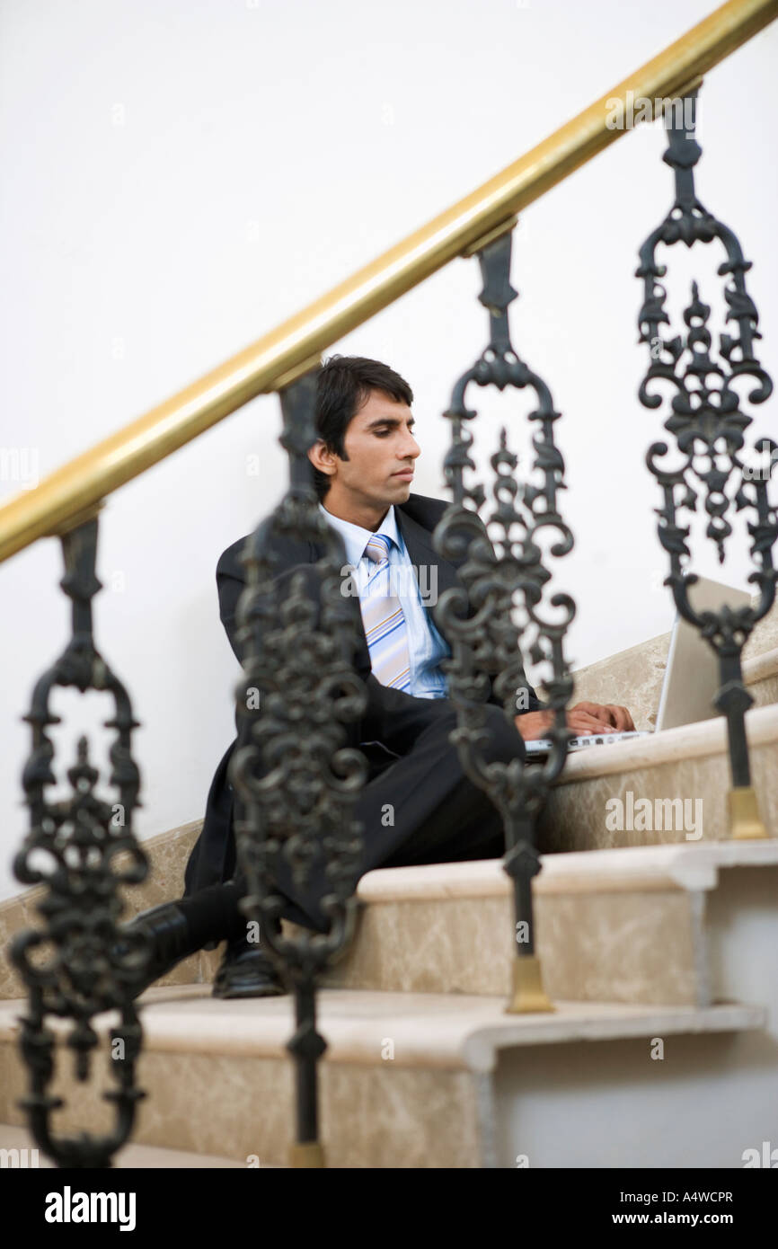 Businessman using laptop on staircase Stock Photo