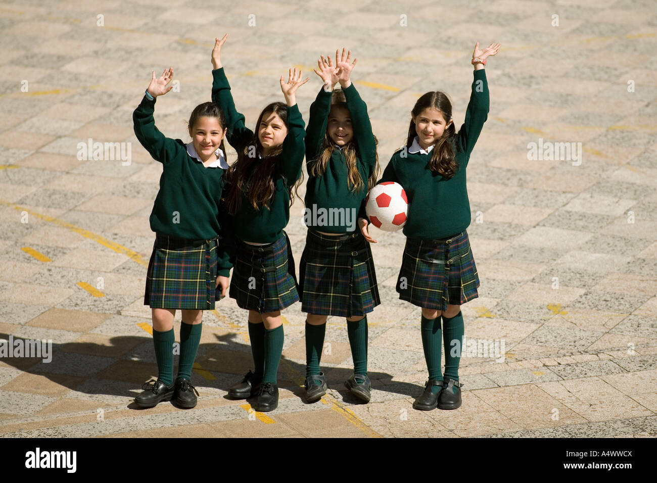 Young students waving while holding soccer ball in courtyard Stock Photo
