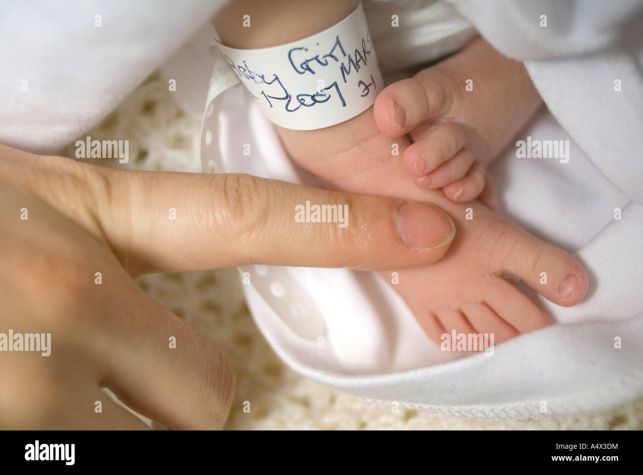 Detail of a newborn baby s feet with identification tag Mothers finger for scale Postnatal labour ward Stock Photo