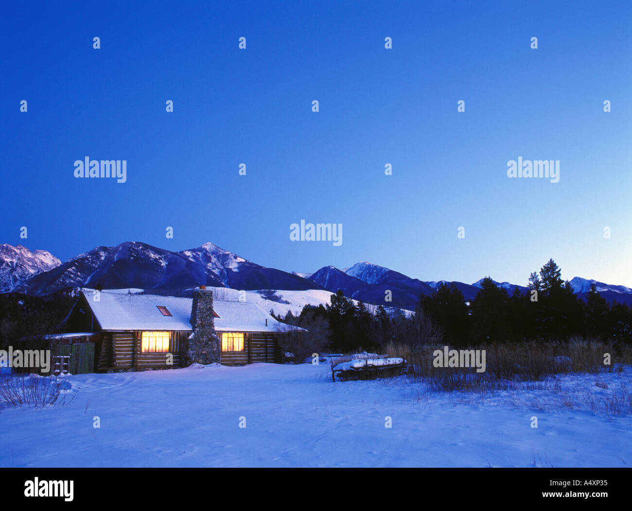 Ranch cabin in winter, windows glowing at twilight Absaroka Mountains in background Paradise Valley Montana USA Property Release Stock Photo