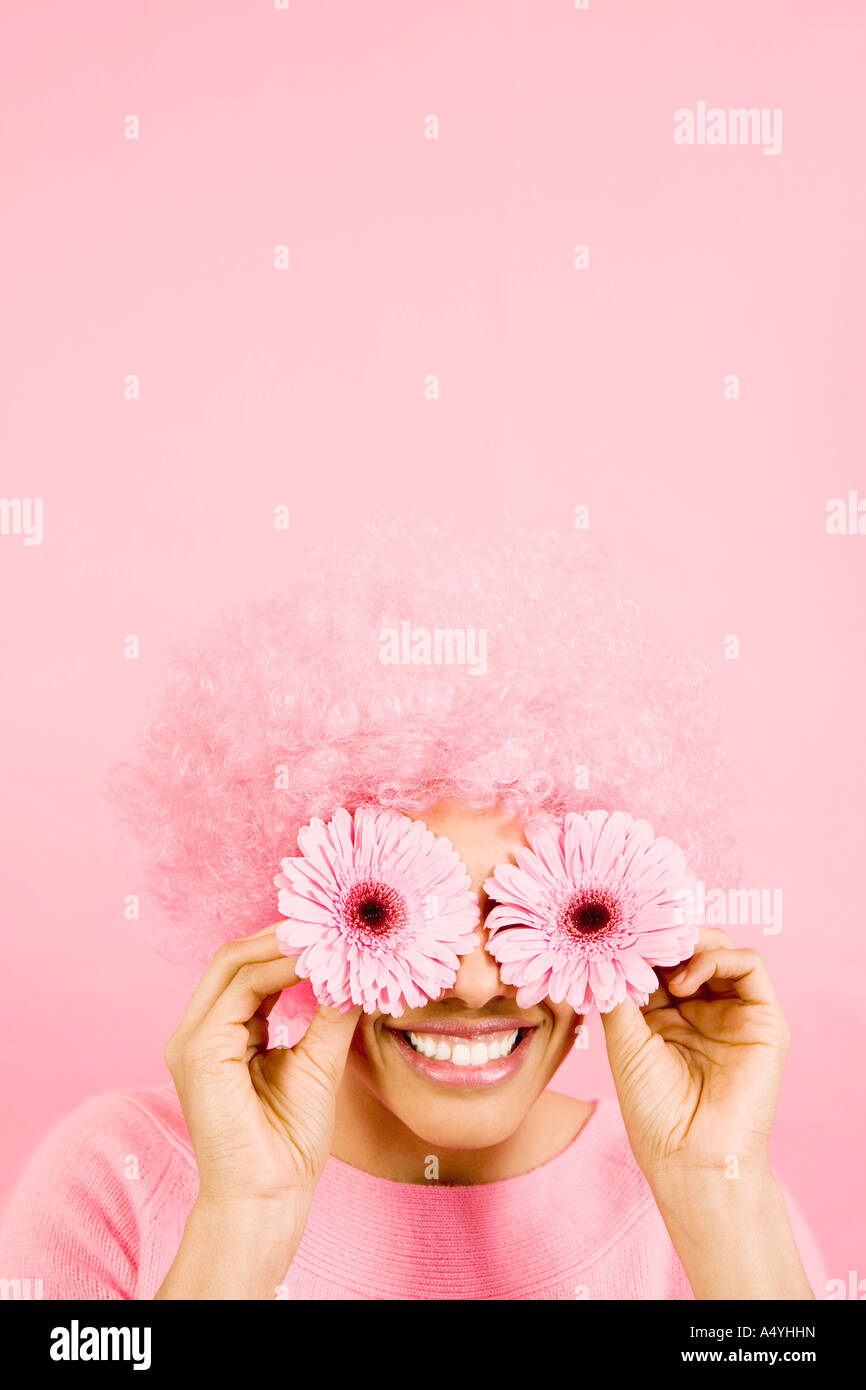 Woman wearing pink wig and holding flowers over eyes Stock Photo